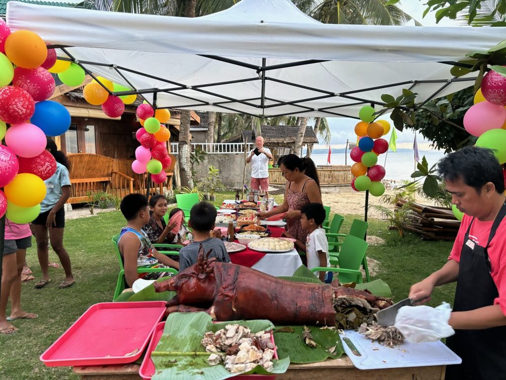 A children's party under a balloon-decked tent, with lechon carved on banana leaves