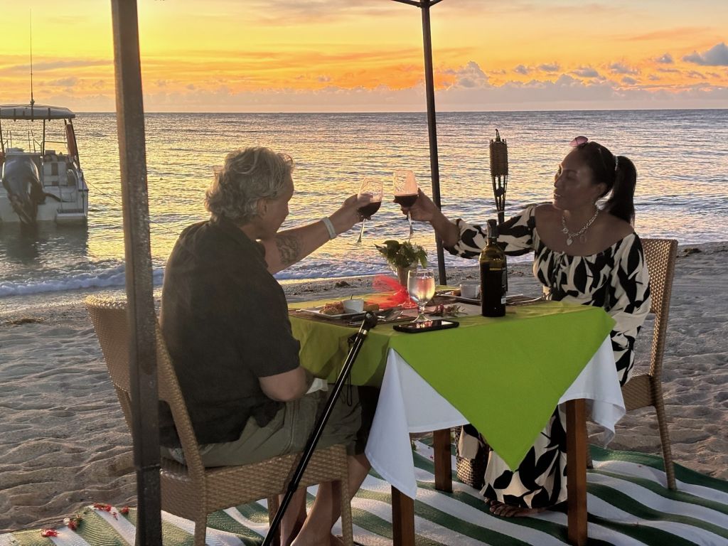 A couple toasting at a candlelit table on the beach at sunset
