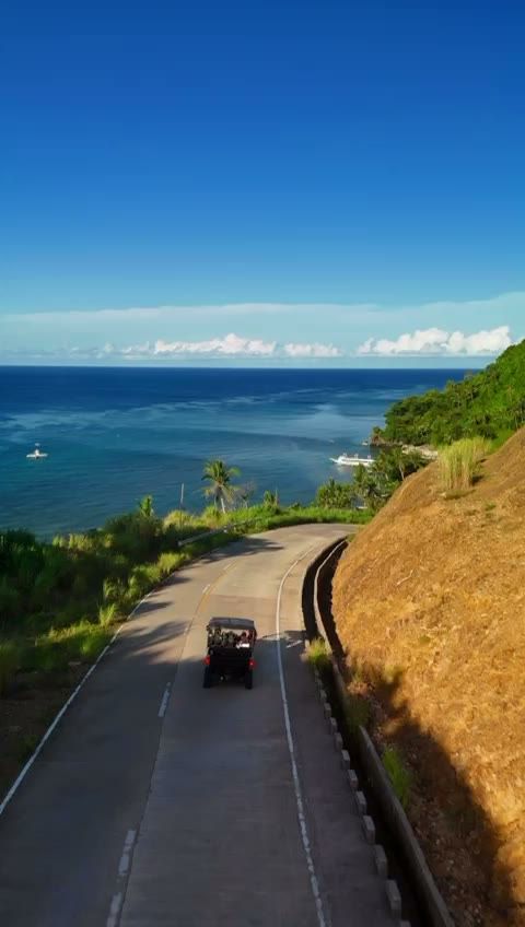 A drone follows our UTV along the coast road of Carabao Island, past green hills, sea views and a village